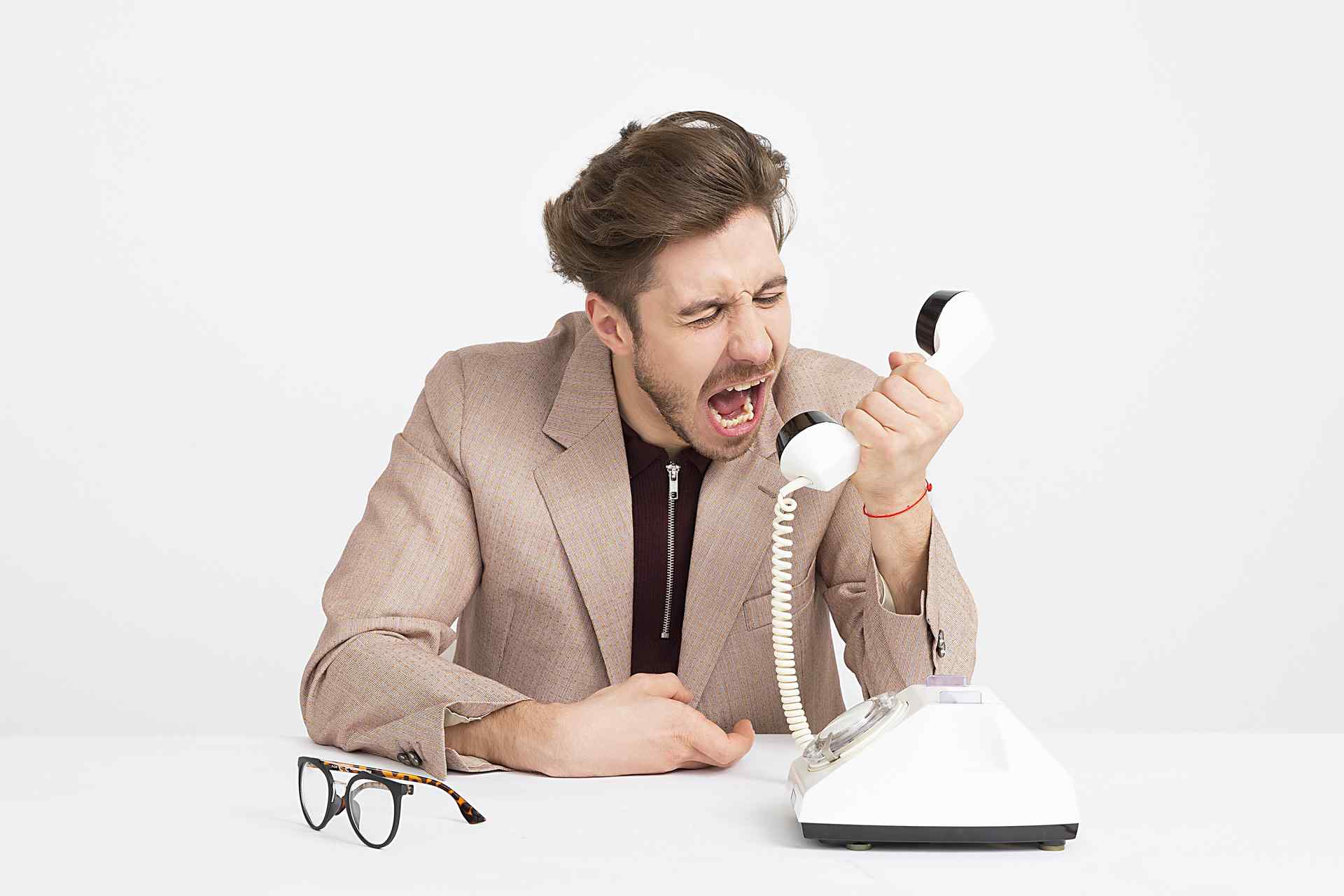 Mężczyzna w średnim wieku przy biurku wrzeszczący z irytacją do słuchawki stacjonarnego telefonu