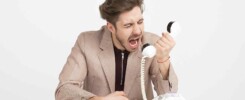 Mężczyzna w średnim wieku przy biurku wrzeszczący z irytacją do słuchawki stacjonarnego telefonu