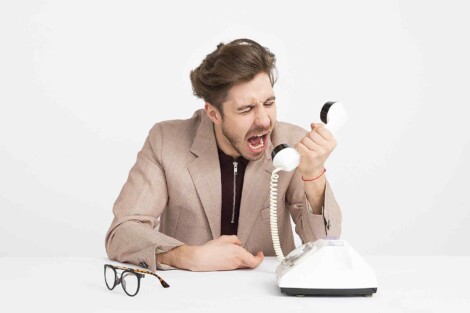 Mężczyzna w średnim wieku przy biurku wrzeszczący z irytacją do słuchawki stacjonarnego telefonu